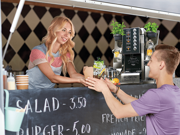 Junge Frau serviert einem jungen Mann ein Getränk von Grapos Brooklyn Streetfood Konzept aus einem Foodtruck